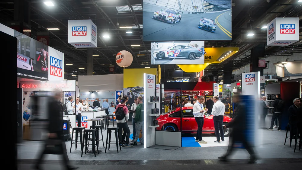 Visiteurs et exposants autour d'une voiture rouge sur le stand LIQUI MOLY.